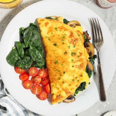 an omelet with spinach and tomatoes on a plate next to a fork