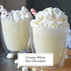 two glasses filled with whipped cream and marshmallows on top of a table