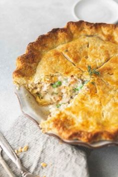 a chicken pot pie on a plate with a fork and knife next to the pie