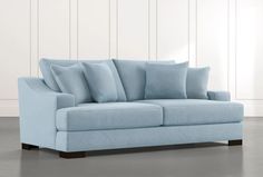 a light blue couch with several pillows on the arm and backrests, against a white wall