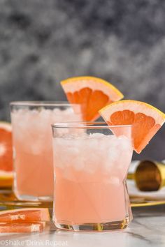 two glasses filled with pink lemonade and garnished with orange slices on a marble table