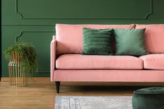 a pink couch with green pillows on it in front of a green wall and wooden floor