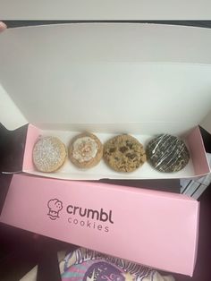 three donuts are in a pink box on the table next to a white box that says crumbl cookies