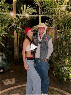 a man and woman standing next to each other in front of palm trees at night