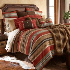 a bed covered in lots of colorful striped comforters and pillows on top of a wooden floor