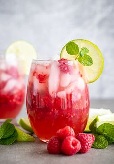 two glasses filled with raspberry lemonade and mint garnish next to sliced limes