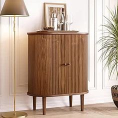 a wooden cabinet sitting next to a lamp and potted plant in a living room