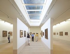 several people are looking at paintings on the wall in an art gallery with skylights