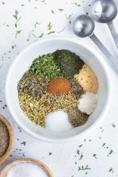 spices and seasonings in a white bowl with spoons next to it on a table