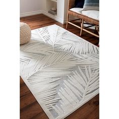 a white rug with palm leaves on it in the middle of a wooden flooring area