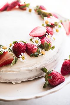 a white cake with strawberries and daisies on the top is decorated with flowers