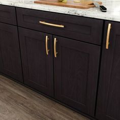 a kitchen with dark wood cabinets and white marble counter tops, gold pulls on the handles