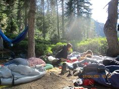 a group of people camping in the woods with hammocks, blankets and sleeping bags