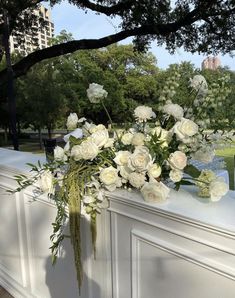 a bouquet of white flowers sitting on top of a wall next to a tree in a park