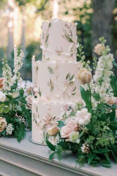 a white wedding cake surrounded by flowers and greenery