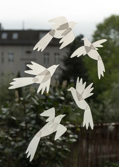 paper cut birds flying in the air over trees and bushes outside an apartment building window