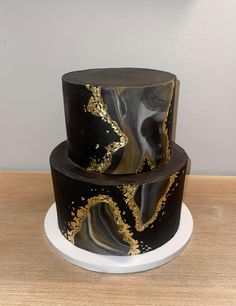 three tiered cake with black and gold designs on top, sitting on a white plate