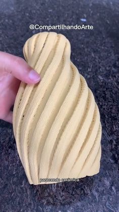 a hand is holding a small piece of yellow clay that looks like wavy lines on the surface