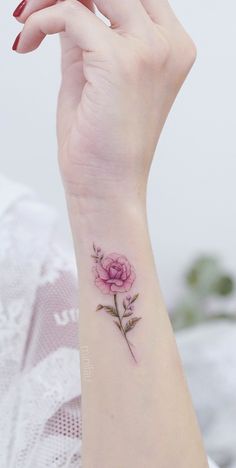 a woman's wrist with a pink rose tattoo on it