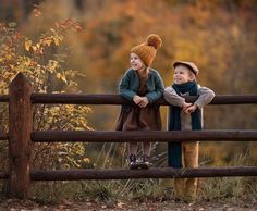 two young boys are standing on a fence looking at each other and one boy is wearing a hat