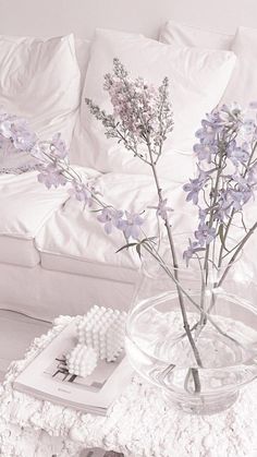 a glass vase filled with purple flowers sitting on top of a table next to a white couch