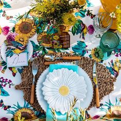 the table is set with sunflowers, plates and utensils on it