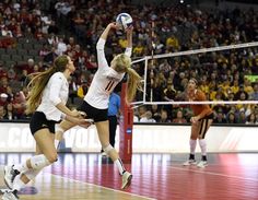 two women playing volleyball on a court with fans in the bleachers behind them