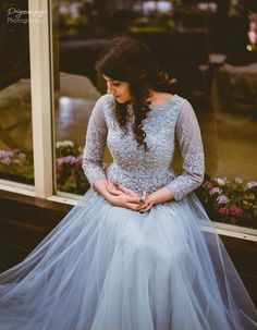 a woman sitting in front of a window wearing a blue dress