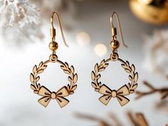 a pair of gold earrings with bows hanging from it's earwires next to a christmas ornament