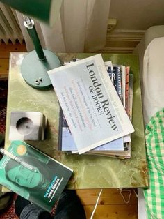 there is a pile of books on top of a table next to a lamp and bed