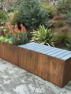 a wooden planter sitting on top of a cement floor next to flowers and plants