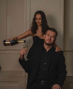 a woman pouring champagne into a man's head while sitting on a chair with his arm around him