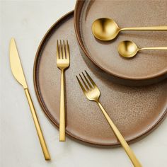 a set of gold colored dinnerware on a white table with utensils and spoons