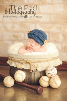 a baby in a basket with baseballs and a bat on the floor next to it