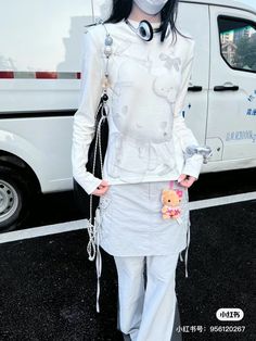 a woman wearing a white outfit and mask standing in front of a van with her hands on her hips