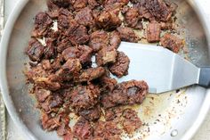 a pan filled with meat and seasoning on top of a table next to a knife