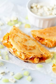 two quesadillas sitting on top of paper next to a bowl of dip