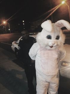 a person dressed in an easter bunny costume standing next to a police car at night