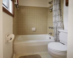 a bath room with a toilet a tub and a shower head mounted to the wall