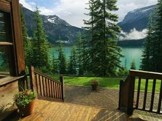 a wooden deck with potted plants on it overlooking a lake and mountains in the distance