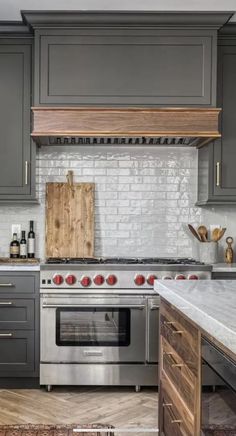 a kitchen with gray cabinets and stainless steel stove top oven, wooden counter tops, and white subway backsplash