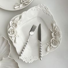 two white plates with flowers and silverware on them, one has a knife and fork