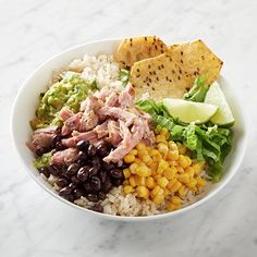 a white bowl filled with rice, beans and corn next to tortilla chips