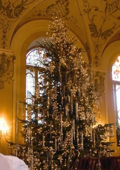 a christmas tree is in the middle of a room with chandeliers and windows