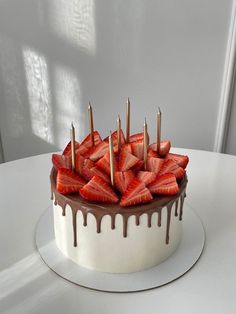 there is a cake with chocolate and strawberries on the top it sits on a white table