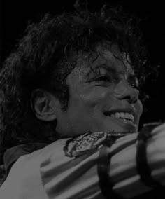 a man with curly hair is smiling and holding a large object in his hand while wearing a white shirt