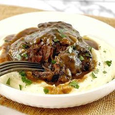 a white plate topped with mashed potatoes covered in beef and gravy next to a fork