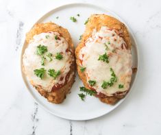 two chicken parmesan sandwiches on a white plate topped with cheese and parsley