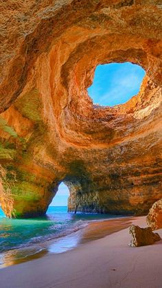 the inside of a cave with blue water and rocks on the beach next to it