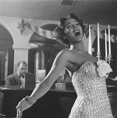 an old photo of a woman singing in front of a piano with candles on it